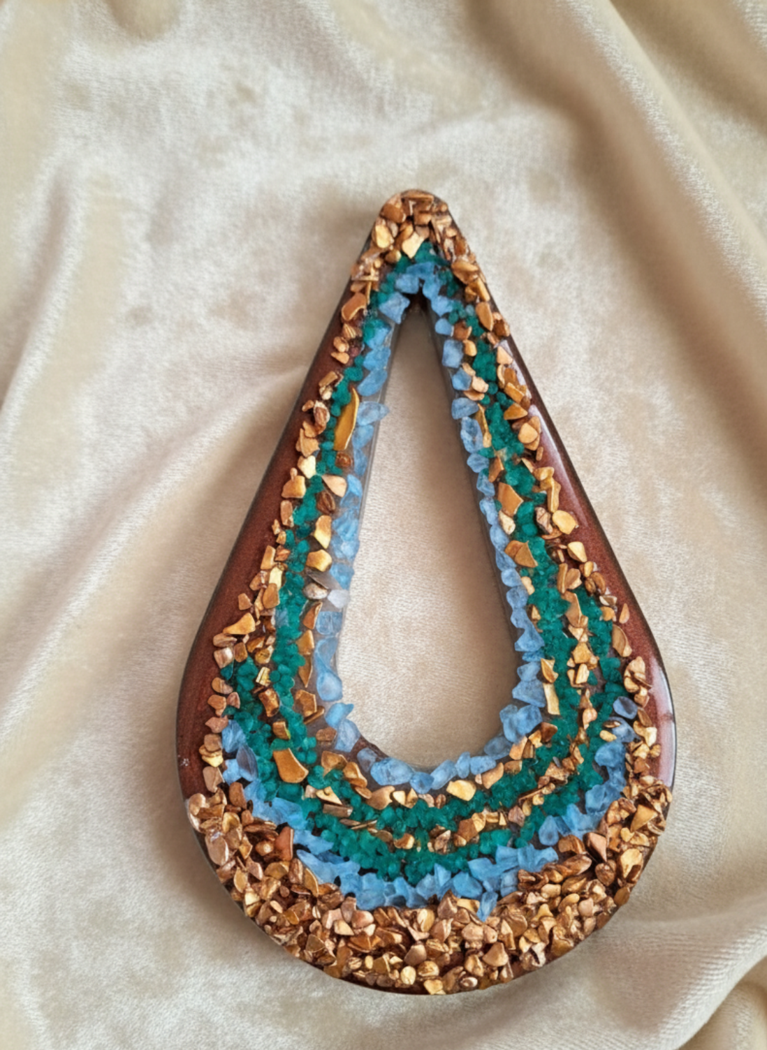 Teardrop-shaped pendant with gold and blue accents on a beige fabric background